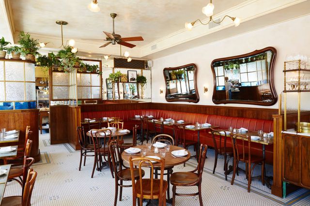 This is a photo of the inside of a restaurant in Brooklyn, with chairs and tables along a wall under a large mirror.